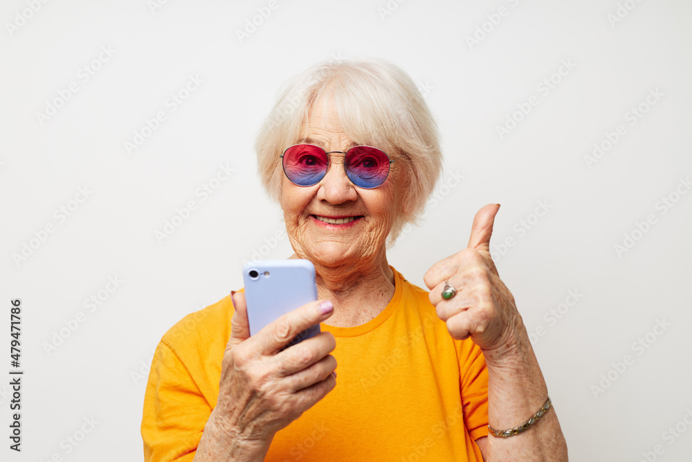 Portrait of an old friendly woman in fashionable glasses with a smartphone in hand close-up emotions
