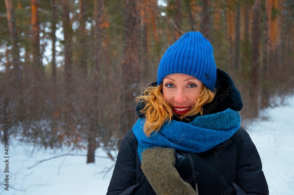 A girl in a blue hat with red lips in winter in a pine forest, a forest in the snow with a blurred background. A girl in a blue hat with red lips in winter in a pine forest, a forest in the snow with a blurred background.