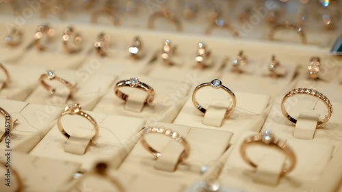 Rows of beautiful expensive fashionable gold rings behind the glass of a jewelry store window shine brightly with their diamonds. Shot in motion. Closeup