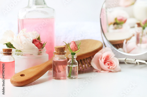 Herbal beauty treatment cosmetic product, fresh delicate pink rose flowers, bathroom shelf with skincare toiletries bottles, haircomb, mirror. Botanical spa body and hair care, soft pastel color