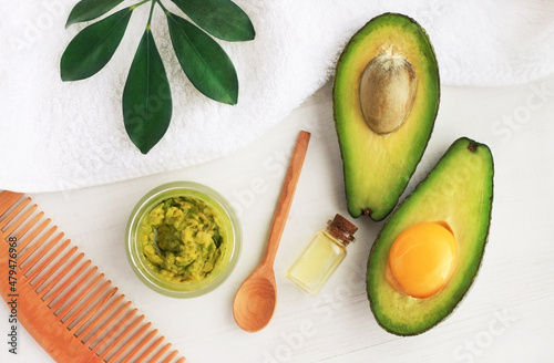 Making homemade hair mask with fresh green avocado and egg yolk ingredients top view white table, natural organic cosmetic product body and facial care, essential oil, haircomb