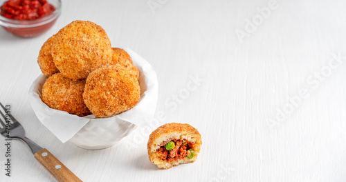 Homemade Arancini Italian rice balls or croquettes deep fried and stuffed with minced beef meat in tomato sauce and green peas served on white wooden table with fork and ketchup. Image with copy space photo