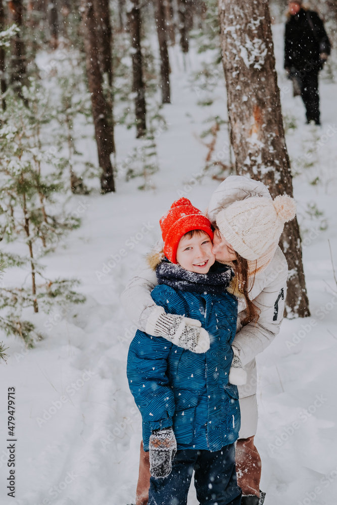 mom kisses her son in the winter forest. Mom walks with her son in a snowfall in the forest. Happy winter holidays with snow. Winter walks in the forest. Mom's love for her son.