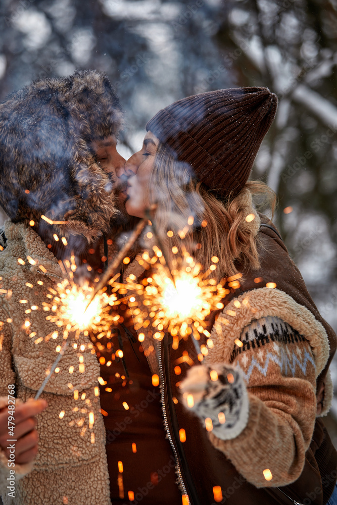 Naklejka premium Couple Love Story in Snow Forest Kissing and Holding Sparklers. Couple in Winter Nature. Couple Celebrating. Valentine's day date.