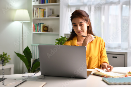 Smiling and feeling positive. happy young Asian woman freelancer working on computer at home. Attractive businesswoman studying online, using laptop software, web surfing information or shopping  photo