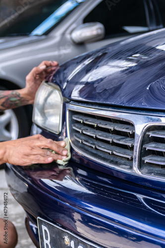 Tattooed man polish and rub a blue car bumper with cloth to get clean , shine and detail on the garage. Suitable for paint work and detailing automotive company background