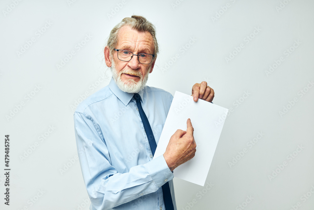 Senior grey-haired man holding documents with a sheet of paper light background Senior grey-haired man holding documents with a sheet of paper light background