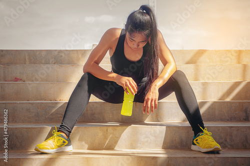 Tired runner woman with a bottle of electrolyte drink freshness after training outdoor workout at the stadium stairway. photo