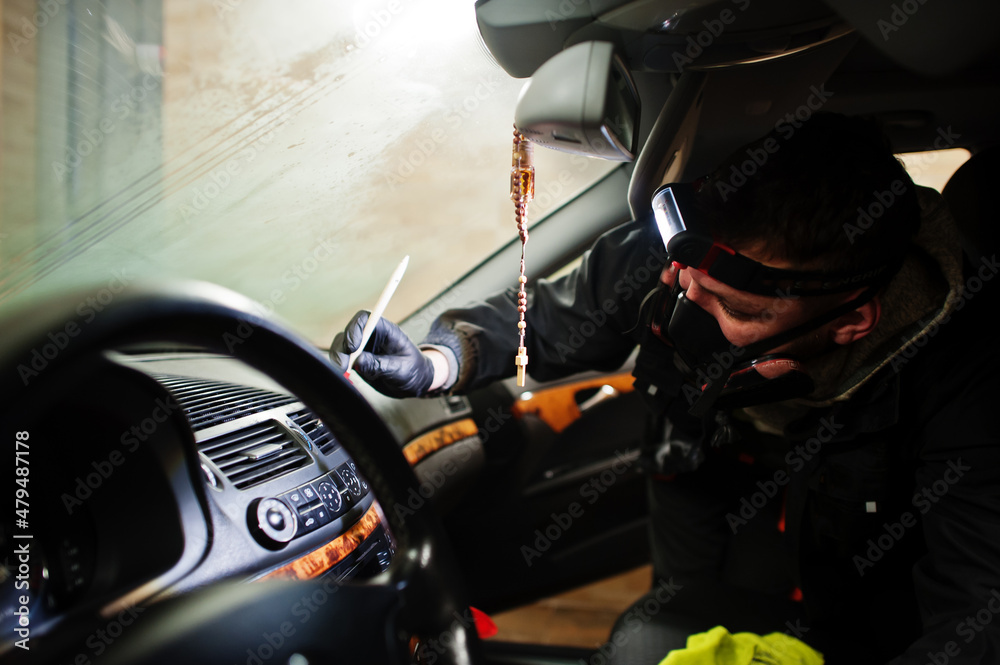 Man in uniform and respirator, worker of car wash center, cleaning car interior cleaning brush . Car detailing concept.