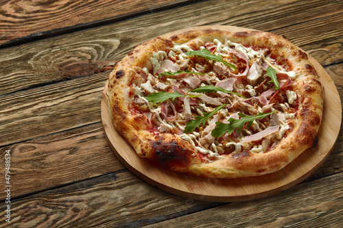 neapolitan Pizza with Mozzarella cheese, bacon, ham, tomato sauce, chicken, Spices and Fresh arugula. Italian pizza on wooden table background