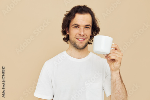 Attractive man with a white mug in his hands emotions posing beige background