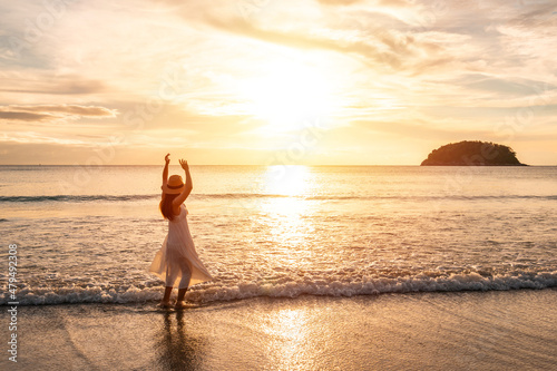 Young woman traveler dancing and enjoying beautiful Sunset on the tranquil beach, Travel on summer vacation concept © Kittiphan