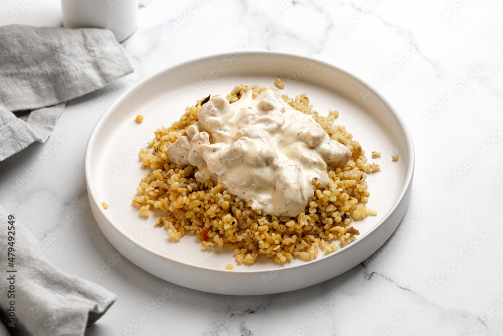 Bulgur with chicken and cream sauce. Dinner idea with bulgur porridge and chicken fillet. White background and white plate Bulgur with chicken and cream sauce. Dinner idea with bulgur porridge and chicken fillet. White background and white plate
