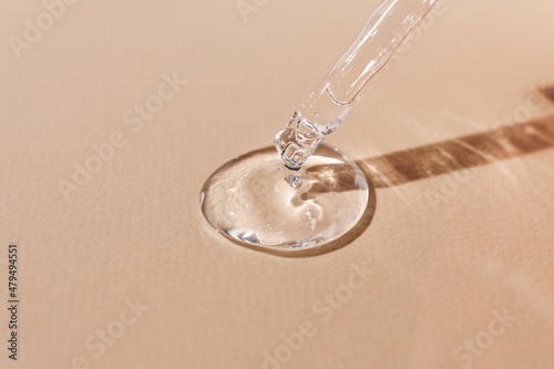 Hyaluronic acid in a glass pipette on a beige background. Transparent serum with beautiful texture close-up, body skin care cosmetic product front view.