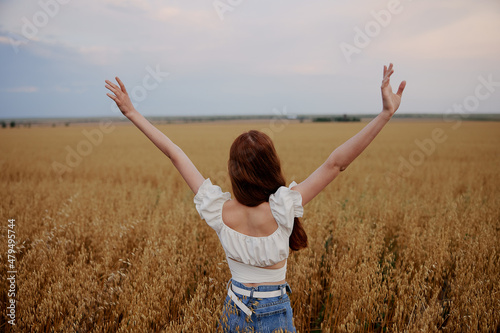 woman with raised up hands in the field admires the landscape back view