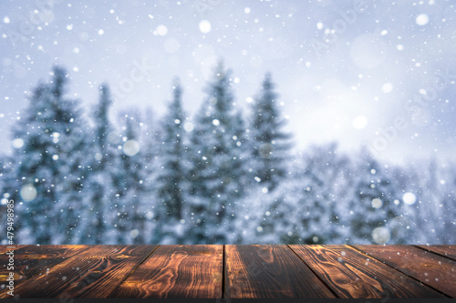 Winter forest with wooden table background. Blurred snow landscape and empty rustic table for product or merchandise.