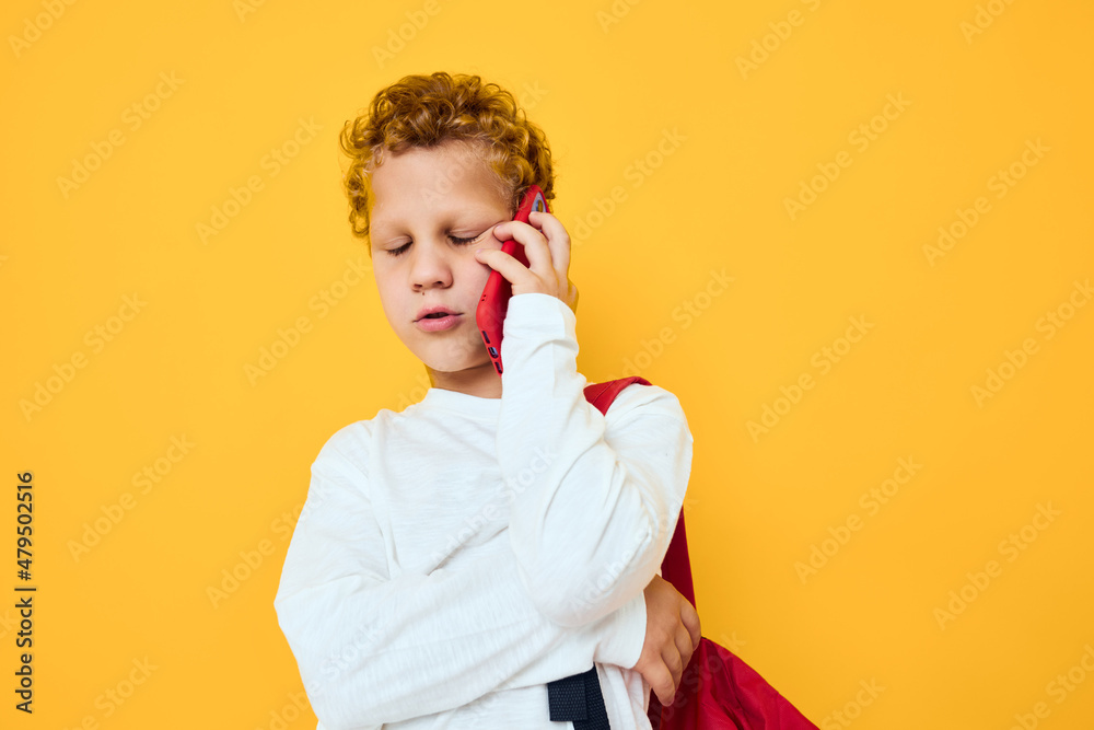 Funny male teen in white sweatshirt mobile cell phone red backpack yellow background