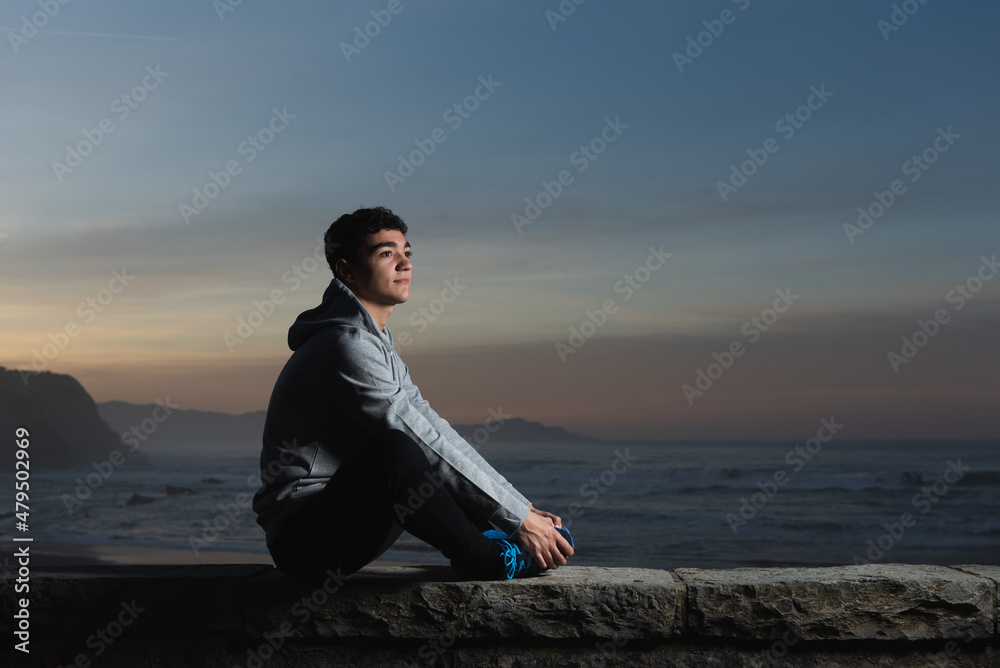Positive hispanic adolescent stretching at sunset, near the coast