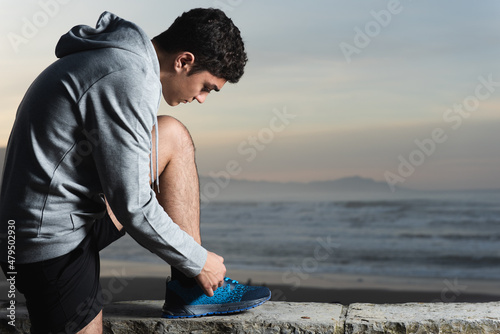 Hispanic teenager tying his sport shoes at seaside.