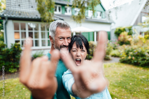 Cheerful heterosexual couple doing horn sign in backyard