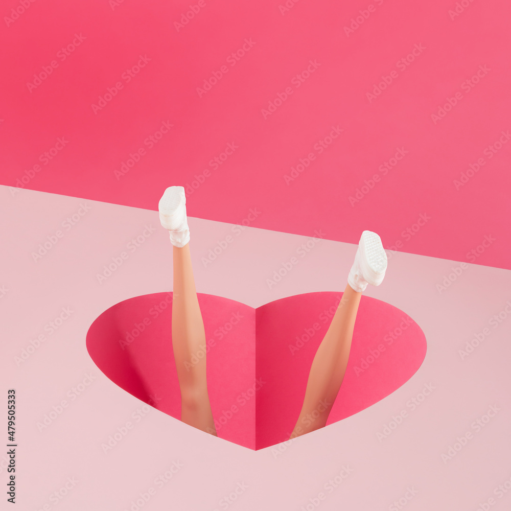 Female doll fell into a heart-shaped hole isolated on pastel pink background. Funny concept of falling in love. Valentine’s Day, Women’s Day or wedding greeting card, invitation card or gift card. 