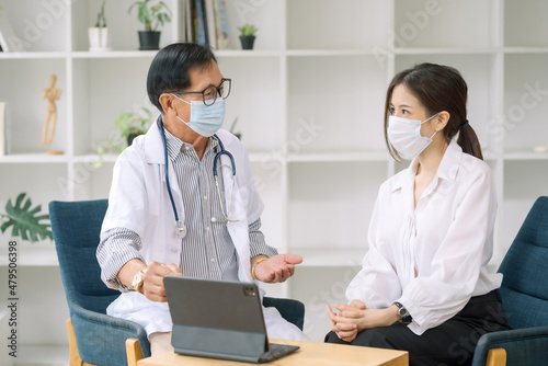 Asian male doctor talking with female patient by using computer tablet. Doctor explains patient treatment information in laptop.