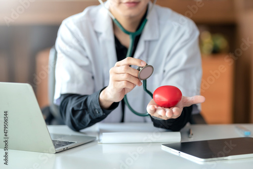 Male doctor holding red heart and stethoscope in the office at hospital. Heart disease treatment concept.