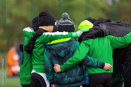 Sports Kids in a Team With Young Coach During Sports Tournament Game on Winter Time. Children in Winter Caps and Jackets Standing in a Team Circle