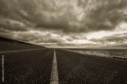 Landscape, seascape sunset on the coast of Huisduinen. The detailed road with white stripe leads to infinity. Black and white, sepia landscape and seascape with street, transportation, long road © Dasya - Dasya