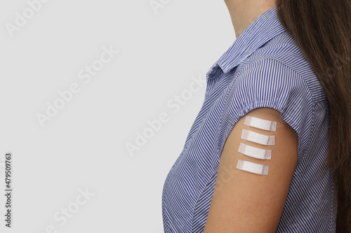 Four medical plasters on the arm of a young woman. Symbol of four doses of covid-19 vaccinations, including booster shots. Free space for text on gray background. Space for a short text on patches.