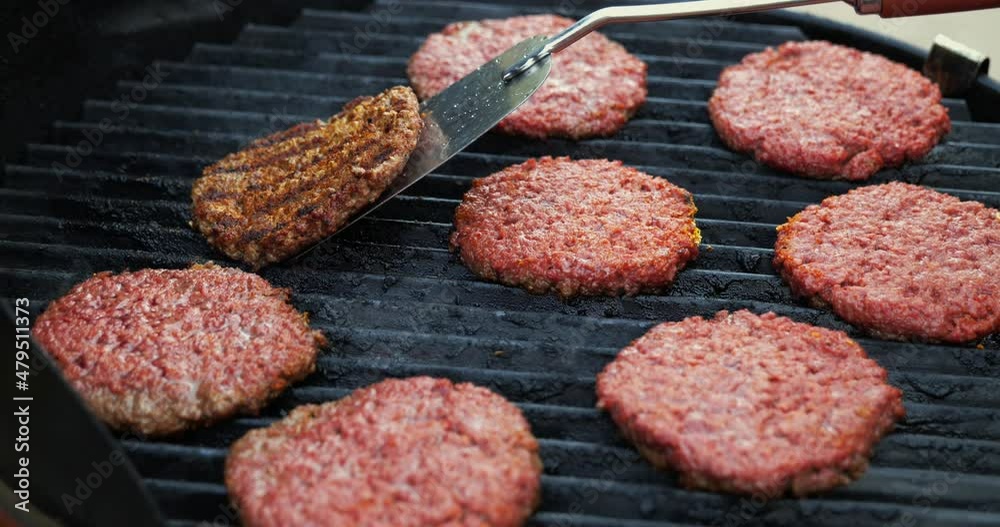 Barbecuing plant based Impossible Burger patties on electric grill wide shot as metal spatula flips burgers to reveal grill lines and brown patty - in Cinema 4k (30fps slowed from 60fps). Barbecuing plant based Impossible Burger patties on electric grill wide shot as metal spatula flips burgers to reveal grill lines and brown patty - in Cinema 4k (30fps slowed from 60fps).