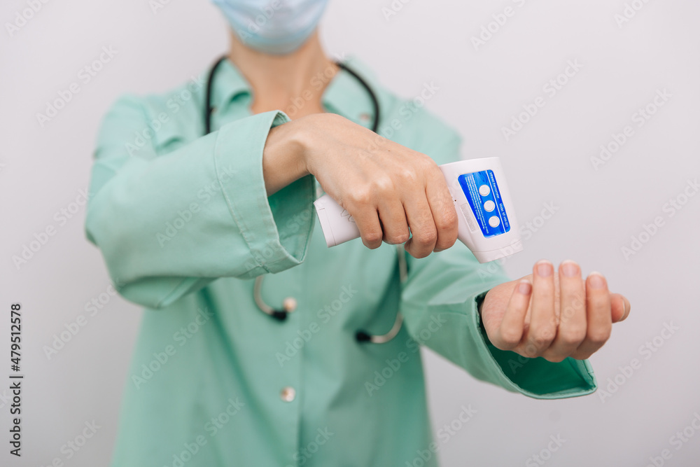 Temperature measurement gun in doctor hands. Close-up shot of doctor wearing protective surgical mask ready to use infrared isometric thermometer gun to check body temperature for virus symptoms Temperature measurement gun in doctor hands. Close-up shot of doctor wearing protective surgical mask ready to use infrared isometric thermometer gun to check body temperature for virus symptoms