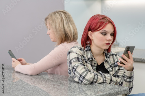 Photos Mother and her teen daughter use smartphones and ignore each other
