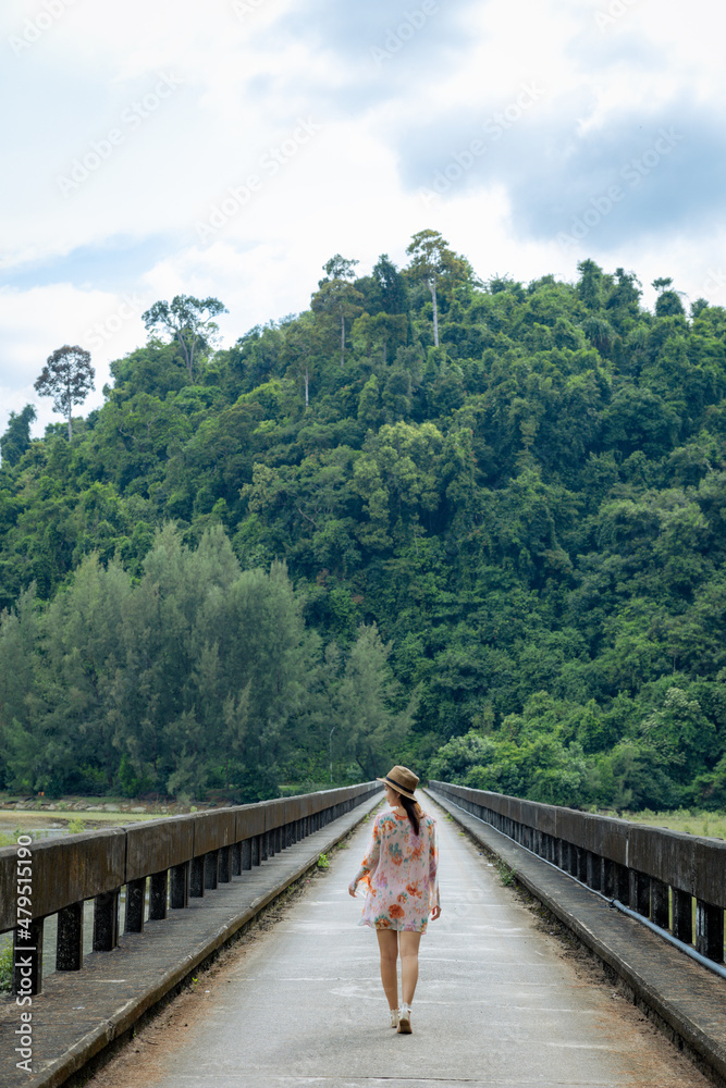 Young woman with hat across bridge over a mountain river in the forest at Laem Son National Park, Ranong, Thailand.