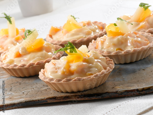 Mini tartas  de crema pastelera y mango sobre tabla de madera. Mini pastry cream and mango tarts on a wooden board.