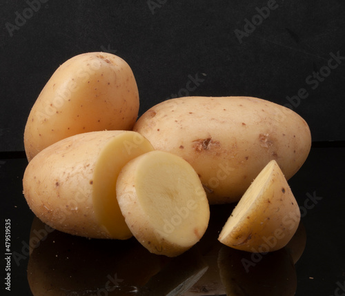 Patatas crudas enteras y cortadas  sobre fondo negro. Whole and sliced ​​raw potatoes on black background. photo