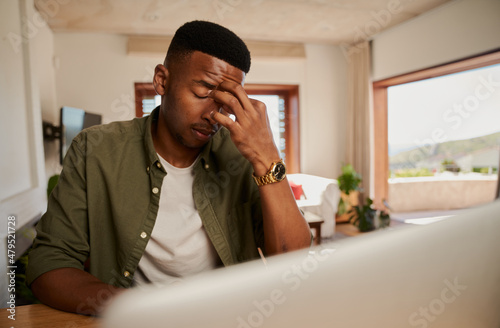 Young adult black male exhausted while he works on laptop from home in modern kitchen.