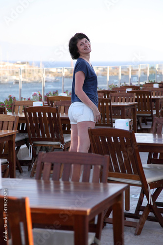 Beautiful smiling woman posing at the camera among the chairs in the restaurant. A woman among the chairs in a cafe. © Master Video