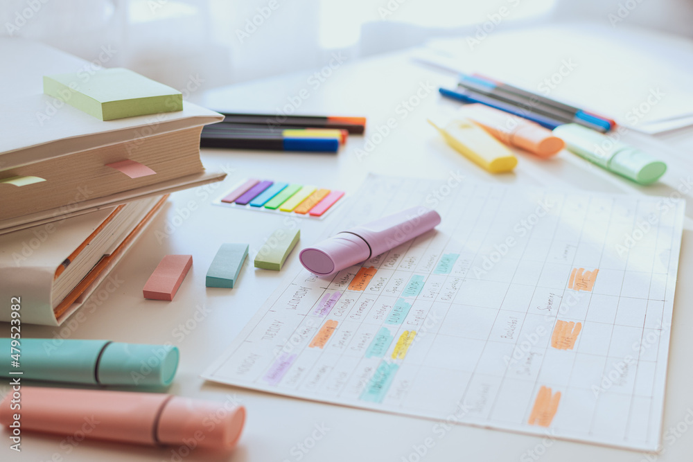 Workplace of a pupil or student. White study table with books and a weekly schedule. Side view. Selective focus. Workplace of a pupil or student. White study table with books and a weekly schedule. Side view. Selective focus.
