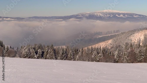 Slow tilt up over magical winter landscape with snowy hill, trees and mountain photo