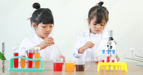 Little girl asian cute little student child learning research and doing a chemical experiment while making analyzing and mixing liquid in test tube at home on the table.
