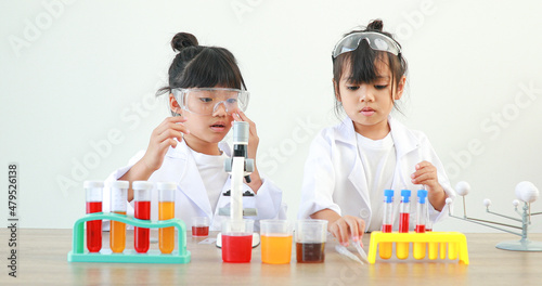 Little girl asian cute little student child learning research and doing a chemical experiment while making analyzing and mixing liquid in test tube at home on the table.