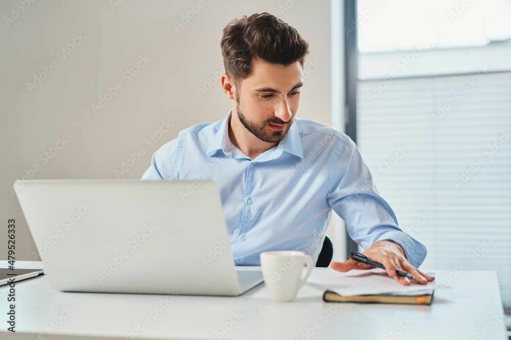 Busy businessman working on laptop looking on document Busy businessman working on laptop looking on document