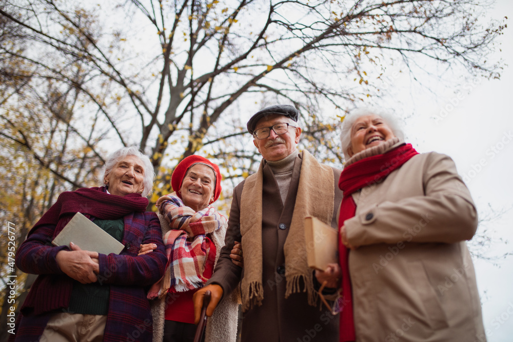 Fototapeta premium Low angle view of group of happy senior friends with books on walk outdoors in park in autumn