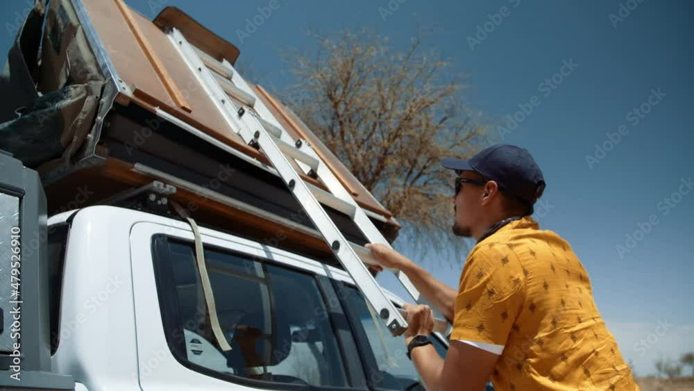 Handheld shot of a tourist as he lowers his rooftop canvas tent of his off road vehicle in Africa. Handheld shot of a tourist as he lowers his rooftop canvas tent of his off road vehicle in Africa.