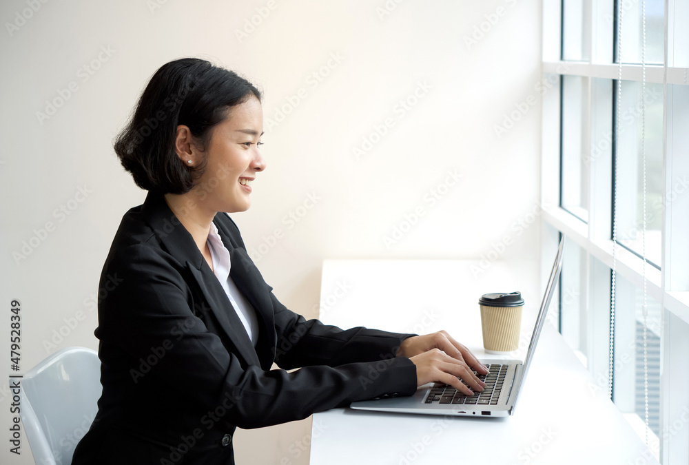 Young asian businesswoman in black suit typing on laptop computer keyboard.