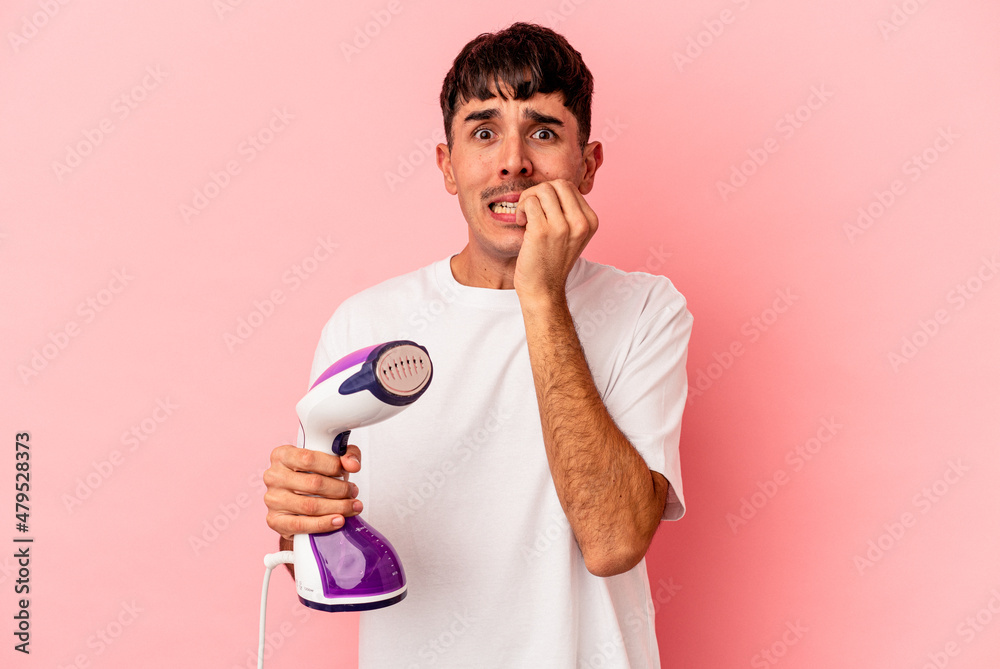 Young mixed race man holding an iron isolated on pink background biting fingernails, nervous and very anxious. Young mixed race man holding an iron isolated on pink background biting fingernails, nervous and very anxious.