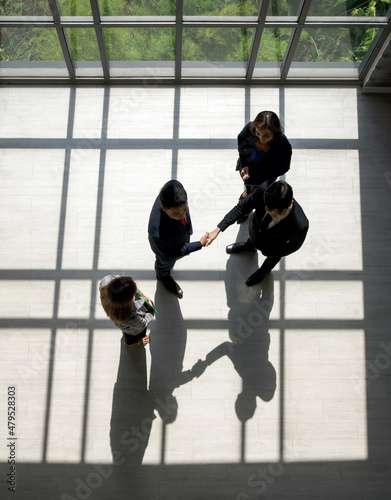 Business partners shaking hands in the modern office. Standing near the window while the sunlight shines on them. There is a shadow on the wooden floor