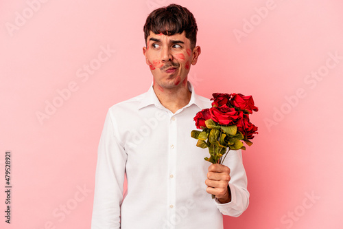 Young mixed race man holding a bouquet of flowers isolated on pink background confused, feels doubtful and unsure.