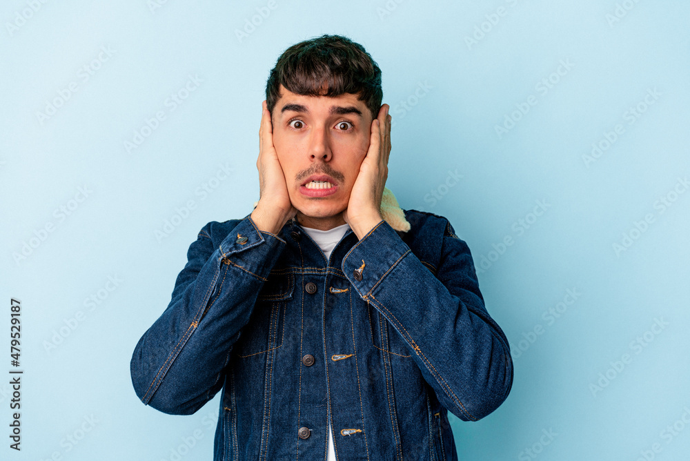 Young mixed race man isolated on blue background covering ears with hands trying not to hear too loud sound.